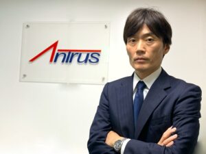 アントラスのロゴが描かれているボードの前で腕を組む代表・髙松の写真