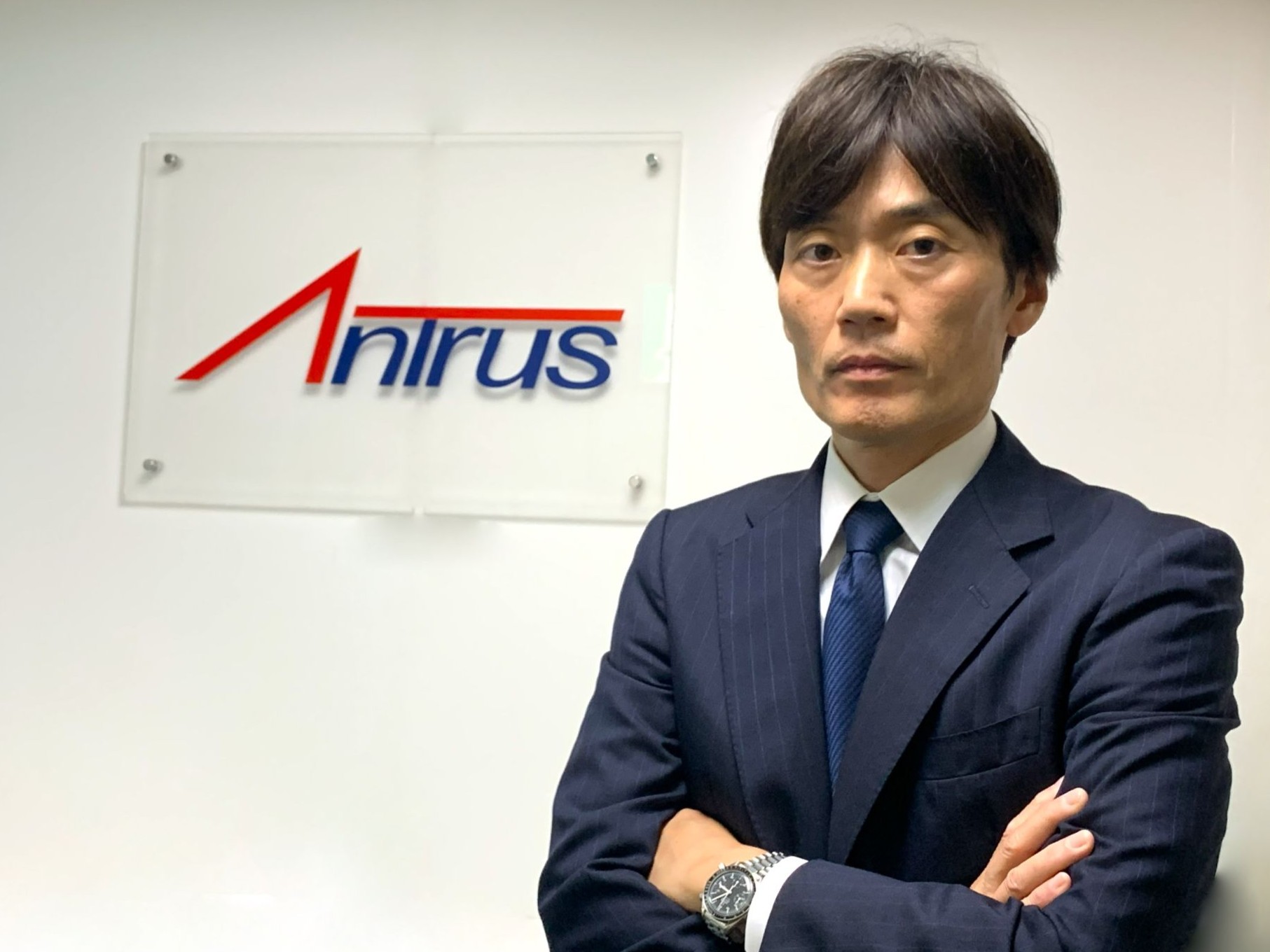 アントラスのロゴが描かれているボードの前で腕を組む代表・髙松の写真